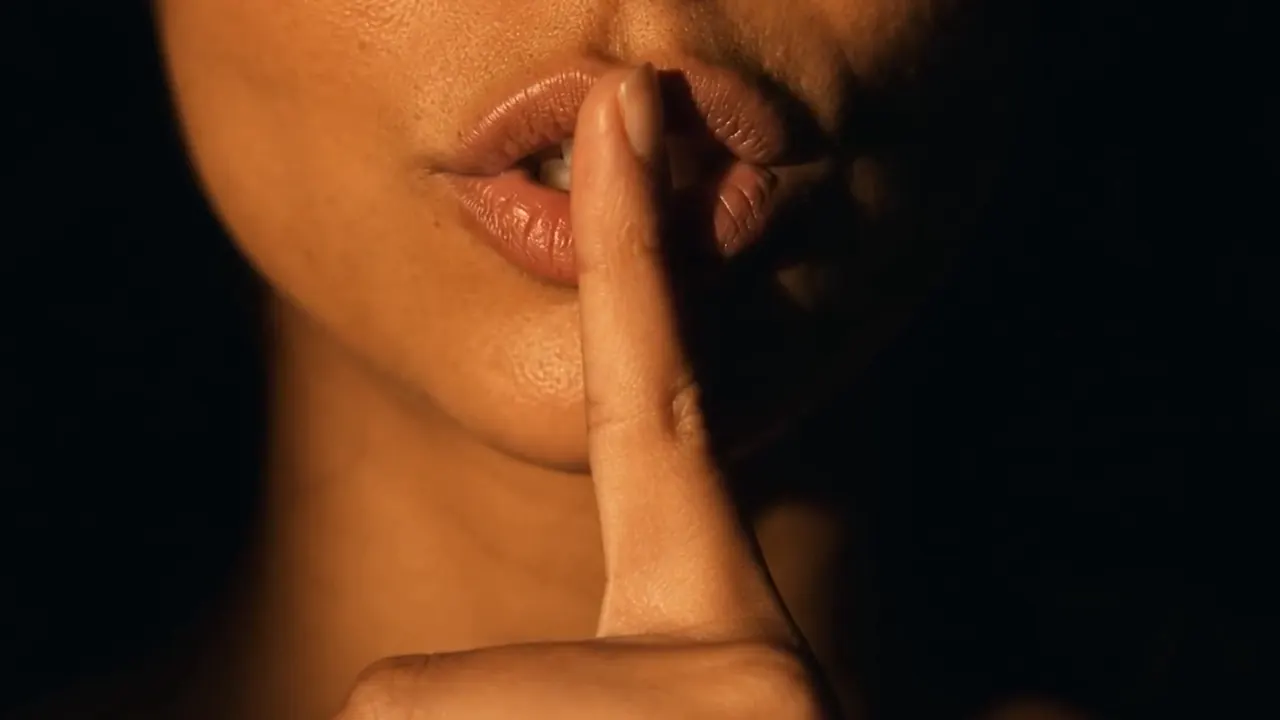 Extreme close-up of a finger held to lips, warm light on black